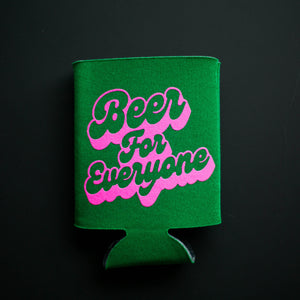 A green drink koolie that says, "Beer for Everyone" in a pink font, laying flat against a black background.
