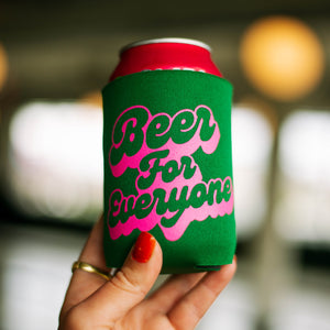 A green drink koolie that says, "Beer for Everyone" in a pink font, being held up by a hand.
