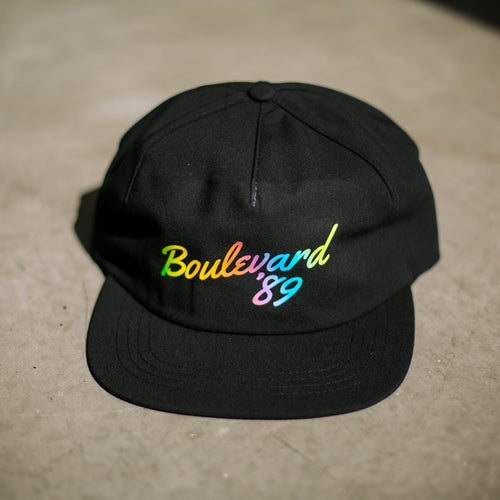 A black cap with rainbow lettering that says, 