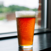 Load image into Gallery viewer, A pint glass full of beer that has a embossed brewery logo
