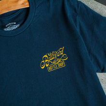 Load image into Gallery viewer, The front of a navy t-shirt with a small yellow lettering in the upper right side.

