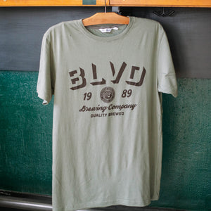 A sage green t-shirt hanging up in bright daylight.