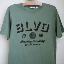 Load image into Gallery viewer, A close up of the black lettering on a sage green t-shirt.
