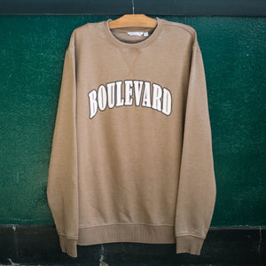 A brown crewneck with faux-embroidered white lettering, hanging up.