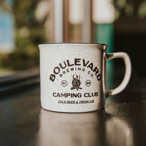 A white enamel mug with black speckles throughout that says, "Boulevard Brewing Co. Camping Club"