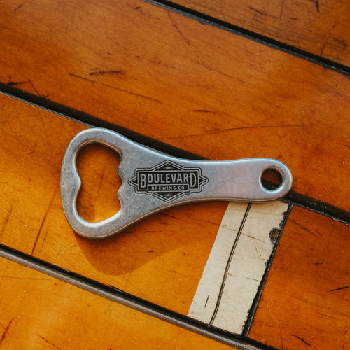 A metal bottle opener with an engraved diamong logo on the handle against a wooden background