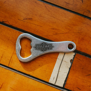 A metal bottle opener with an engraved diamong logo on the handle against a wooden background