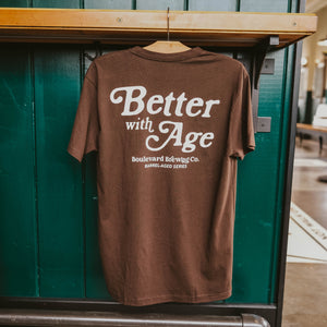 The Back of a brown t-shirt, that says, "Better with Age, Boulevard Brewing Co., Barrel-Aged Series" in a white font, hanging up.