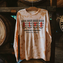 Load image into Gallery viewer, A brown and peach tie-dyed long sleeve with BLVD spelled out on barrels, hanging in front of barrels.
