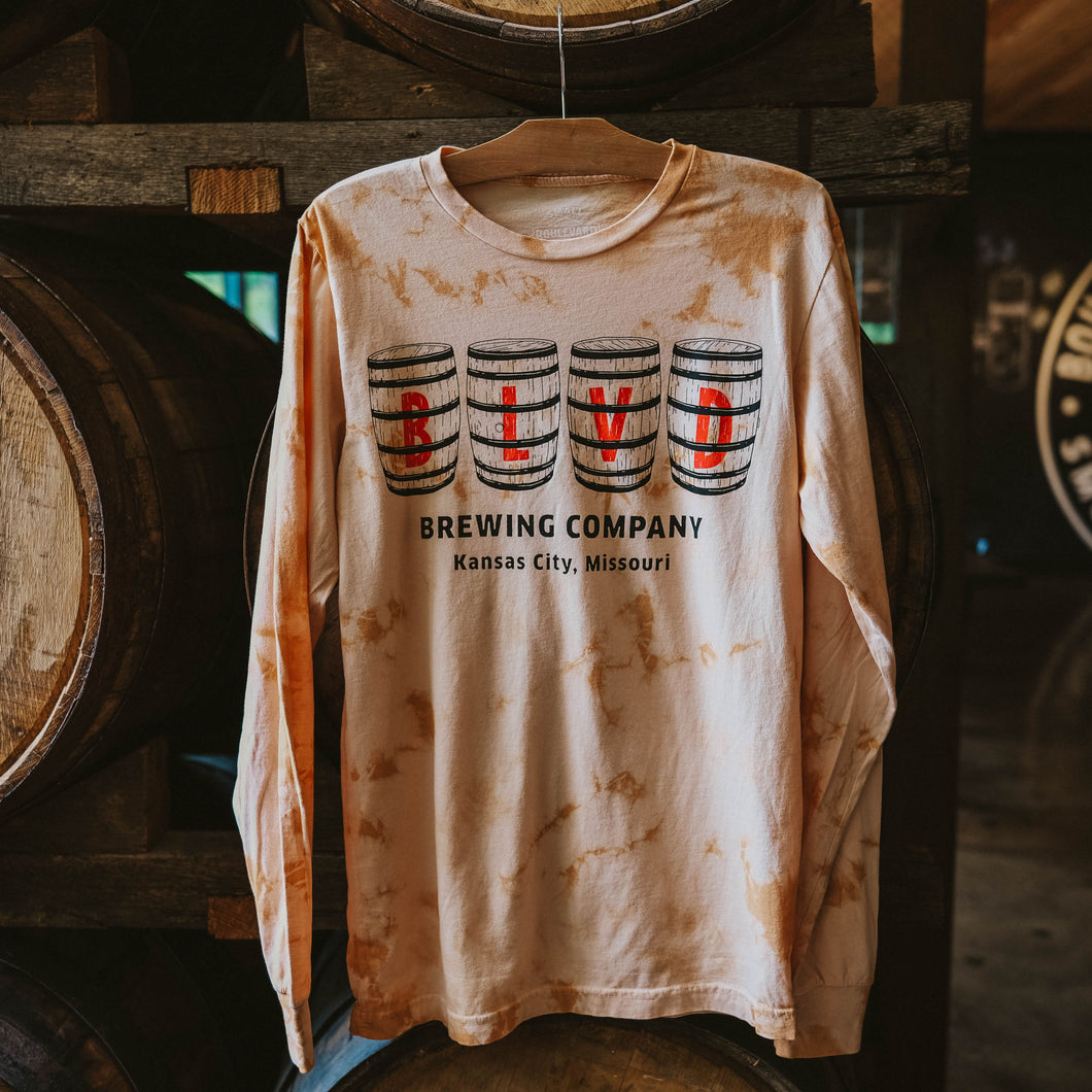A brown and peach tie-dyed long sleeve with BLVD spelled out on barrels, hanging in front of barrels.