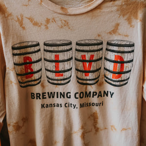 A close up of the logo on a  brown and peach tie-dyed long sleeve with BLVD spelled out on barrels.