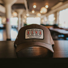 Load image into Gallery viewer, A brown trucker cap with a white patch, spelling BLVD out in barrels.
