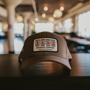 A brown trucker cap with a white patch, spelling BLVD out in barrels.
