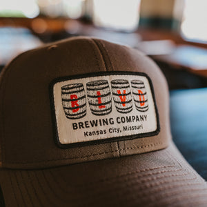 A sideview of a brown trucker cap with a white patch, spelling BLVD out in barrels.