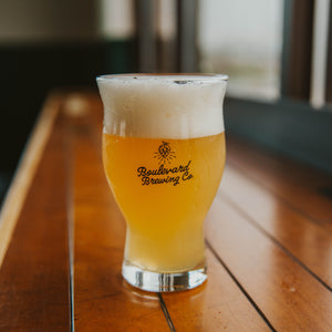 A glass with a large bowl and flared top full of light beer that says, "Boulevard Brewing Co." in a cursive font with a hop above the text