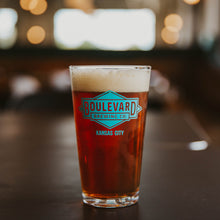 Load image into Gallery viewer, A pint glass full of amber beer with a teal diamond logo
