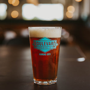 A pint glass full of amber beer with a teal diamond logo