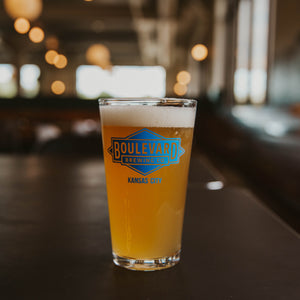 A pint glass full of light beer with a blue diamond logo