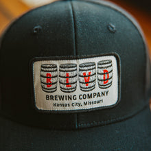 Load image into Gallery viewer, A close-up of a black trucker cap with a white patch, spelling BLVD out in barrels.
