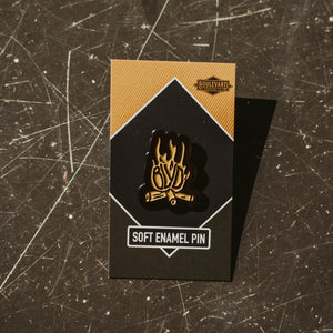 A flame-shaped enamel pin on its backing, on a grey background.