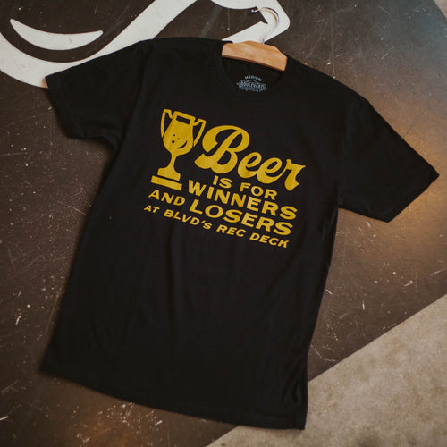 A black t-shirt, laying on the shuffleboard lanes,  with gold font, that says, 