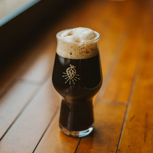 A glass full of a dark beer that has a gold hop