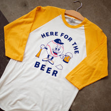 Load image into Gallery viewer, A yellow and white raglan tee with a baseball character carrying a beer and baseball bat that says, Here for the Beer, laying on the floor.
