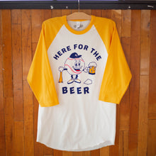 Load image into Gallery viewer, A yellow and white raglan tee with a baseball character carrying a beer and baseball bat that says, Here for the Beer, hanging up.
