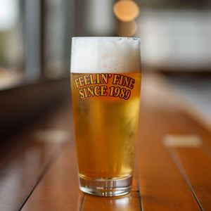 A tall glass full of light beer that says, "Feelin' Fine Since 1989" in yellow letters