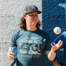 Load image into Gallery viewer, Person wearing a Kansas City-themed t-shirt and cap, holding a can and a baseball, against a textured wall.
