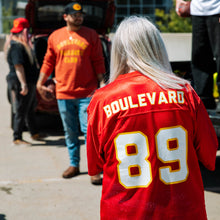 Load image into Gallery viewer, The back of a grey-haired woman wearing the jersey at a parking lot tailgate.
