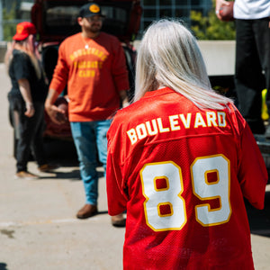 The back of a grey-haired woman wearing the jersey at a parking lot tailgate.