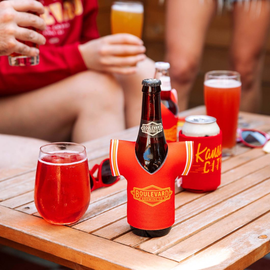 A beer dressed in a red koolie shaped as a football jersey with a yellow Boulevard diamond logo, sitting on a table