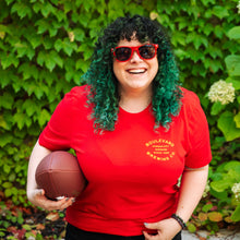 Load image into Gallery viewer, A smiling girl modeling the red barrel stamp tee, holding a football
