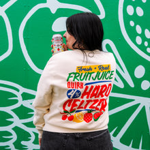 Load image into Gallery viewer, Person wearing a colorful sweatshirt with text and graphics, holding a can against a green wall with white designs.
