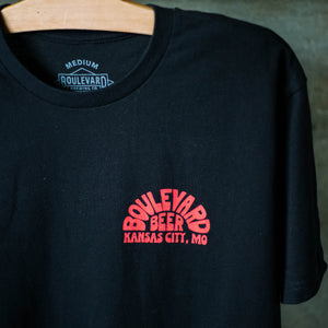 A small red logo in the upper right corner on the front of a black t-shirt.