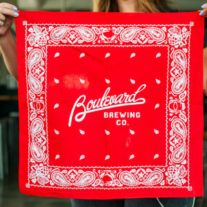 A woman holding up a red and white bandana that says, "Boulevard Brewing Co." in the middle of it.