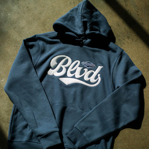 A navy hoodie with white BLVD embroidered lettering and a front kangaroo pocket, laying on the ground.