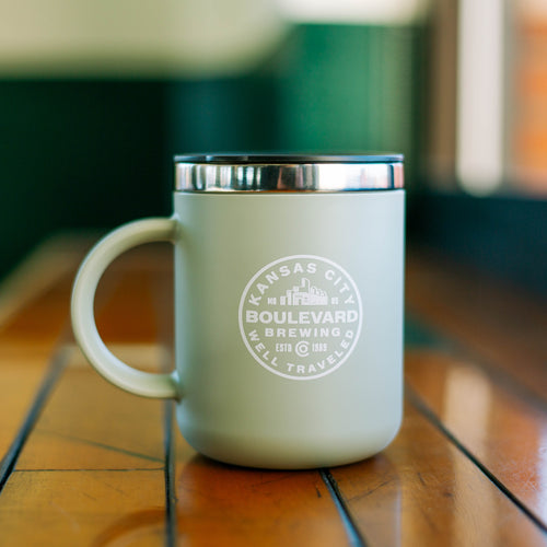 A  mint green travel mug with a metal rim that has a boulevard circle logo in the middle