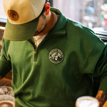 Load image into Gallery viewer, Person wearing a green jacket with a logo, holding a cup in a casual setting.
