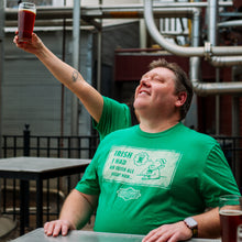 Load image into Gallery viewer, Man in a green t-shirt holding a glass of beer outdoors
