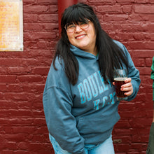 Load image into Gallery viewer, Person wearing a blue hoodie with 'Boulder' text, holding a glass of dark liquid against a brick wall.
