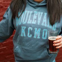 Load image into Gallery viewer, Person wearing a 'Boulevard KC MO' hoodie holding a glass of beer against a red brick wall.
