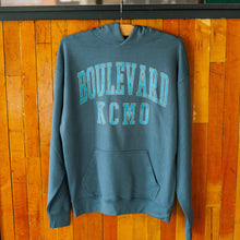 Load image into Gallery viewer, Blue hoodie with 'BOULEVARD KCMO' text on a wooden background
