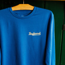 Load image into Gallery viewer, Blue long sleeve shirt with 'Boulevard' logo on a wooden hanger against a green wall.
