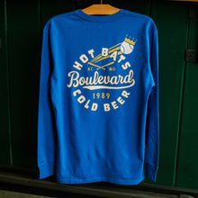 Load image into Gallery viewer, Blue long-sleeve shirt with text and graphics on a wooden surface against a green wall.
