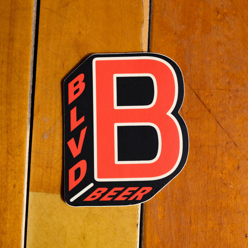 A red and black B-shaped sticker on a wood floor.