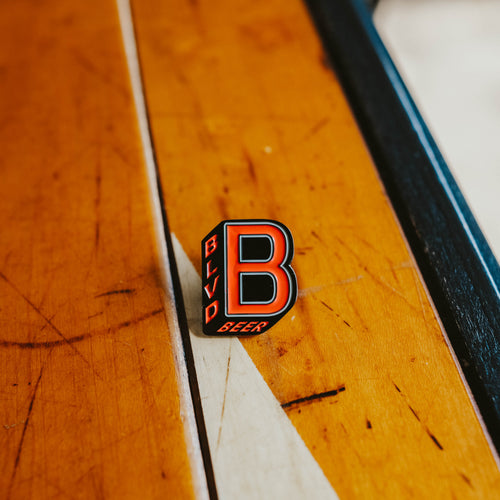 A red and black B-Shaped enamel pin on a table.