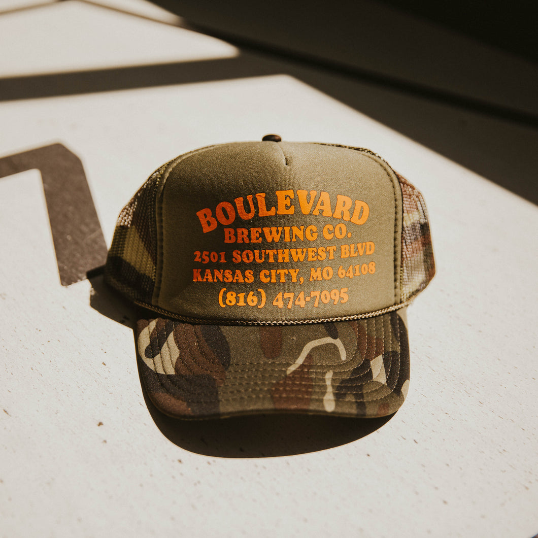 A foam camo print trucker cap with orange lettering. 