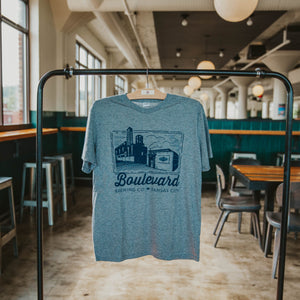A grey t-shirt with a navy image of the brewery, hanging on a rack.